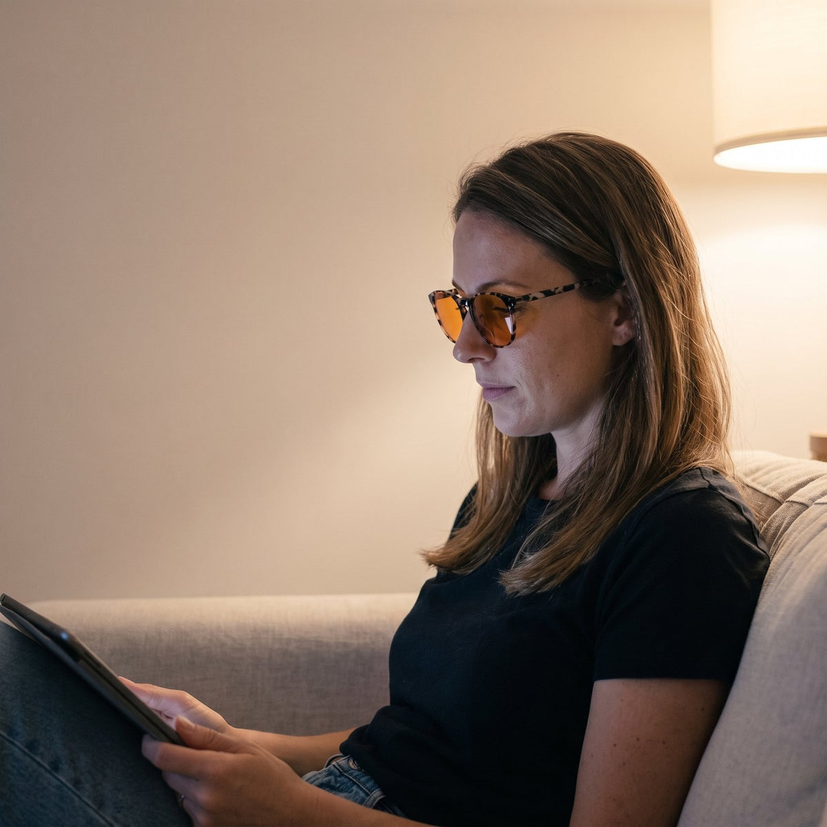 A woman reading a tablet on a sofa wearing Hueban SR Nomad glasses